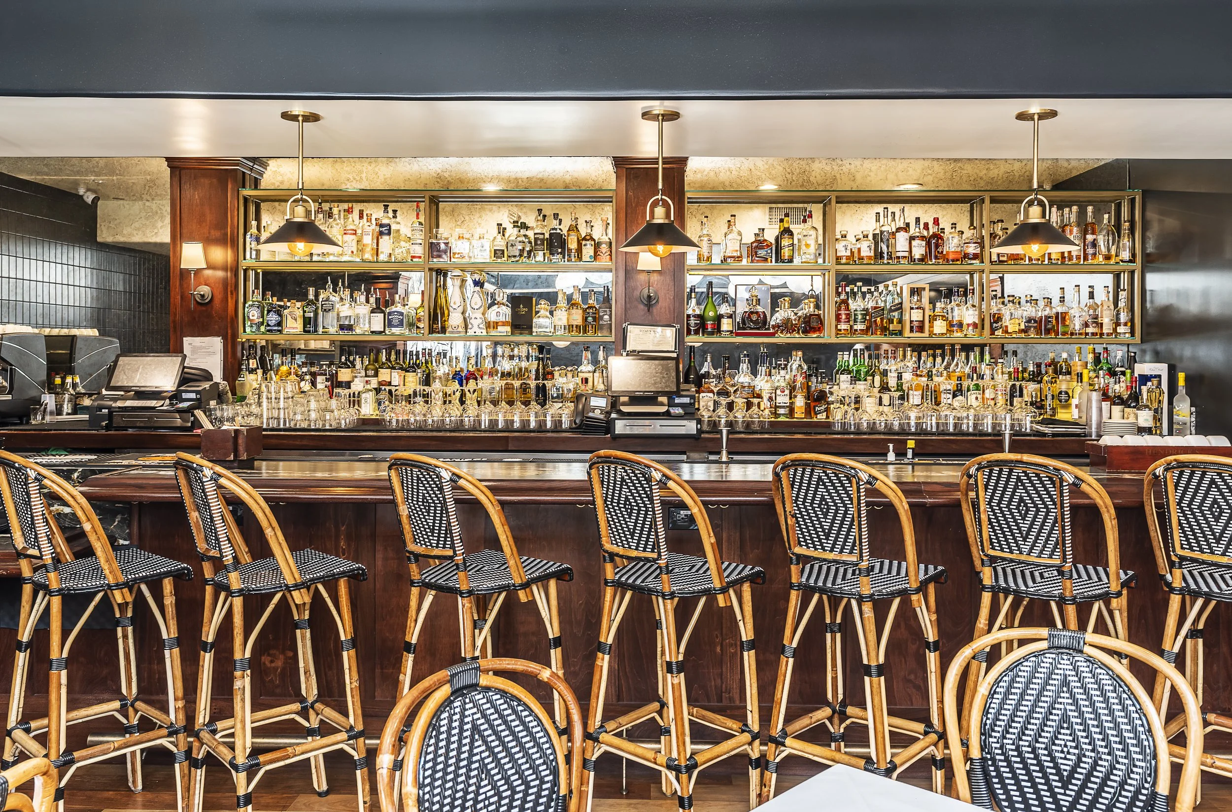 Elegant bar at Lucky’s Steakhouse in Malibu with wooden accents, well-stocked shelves of liquor, and wicker bar stools, creating a sophisticated atmosphere for patrons.