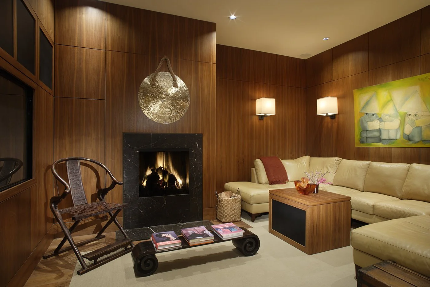 A cozy living room with a warm fireplace, wooden panel walls, and comfortable seating.