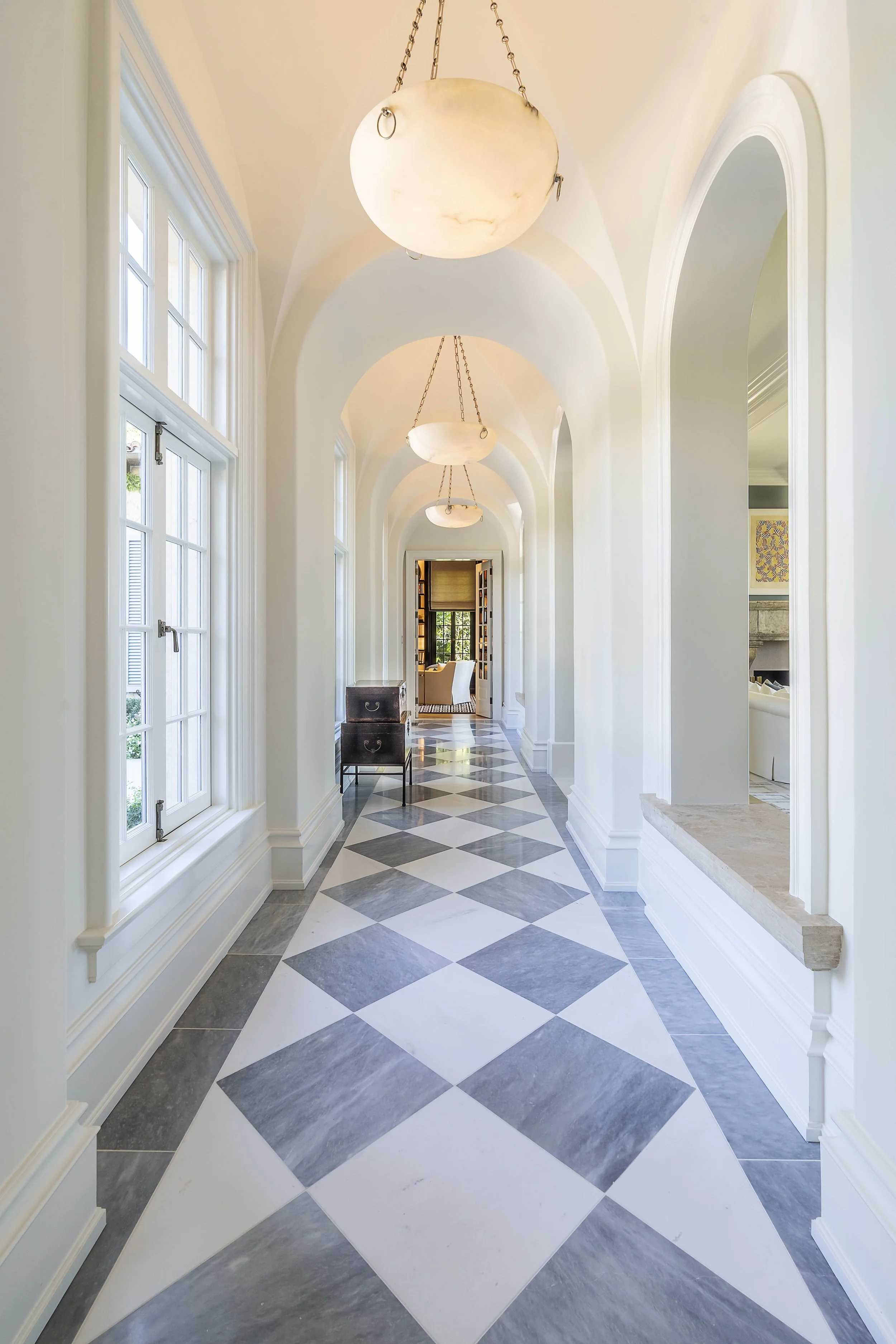 Elegant hallway with arched ceiling, large windows, patterned floor tiles, and spherical pendant lights.