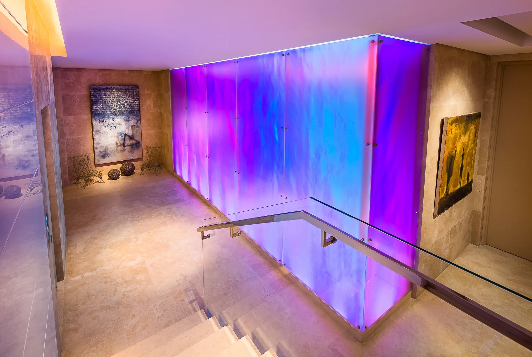 Illuminated staircase with a vibrant blue and purple feature wall, adding a modern artistic touch to the contemporary interior design.