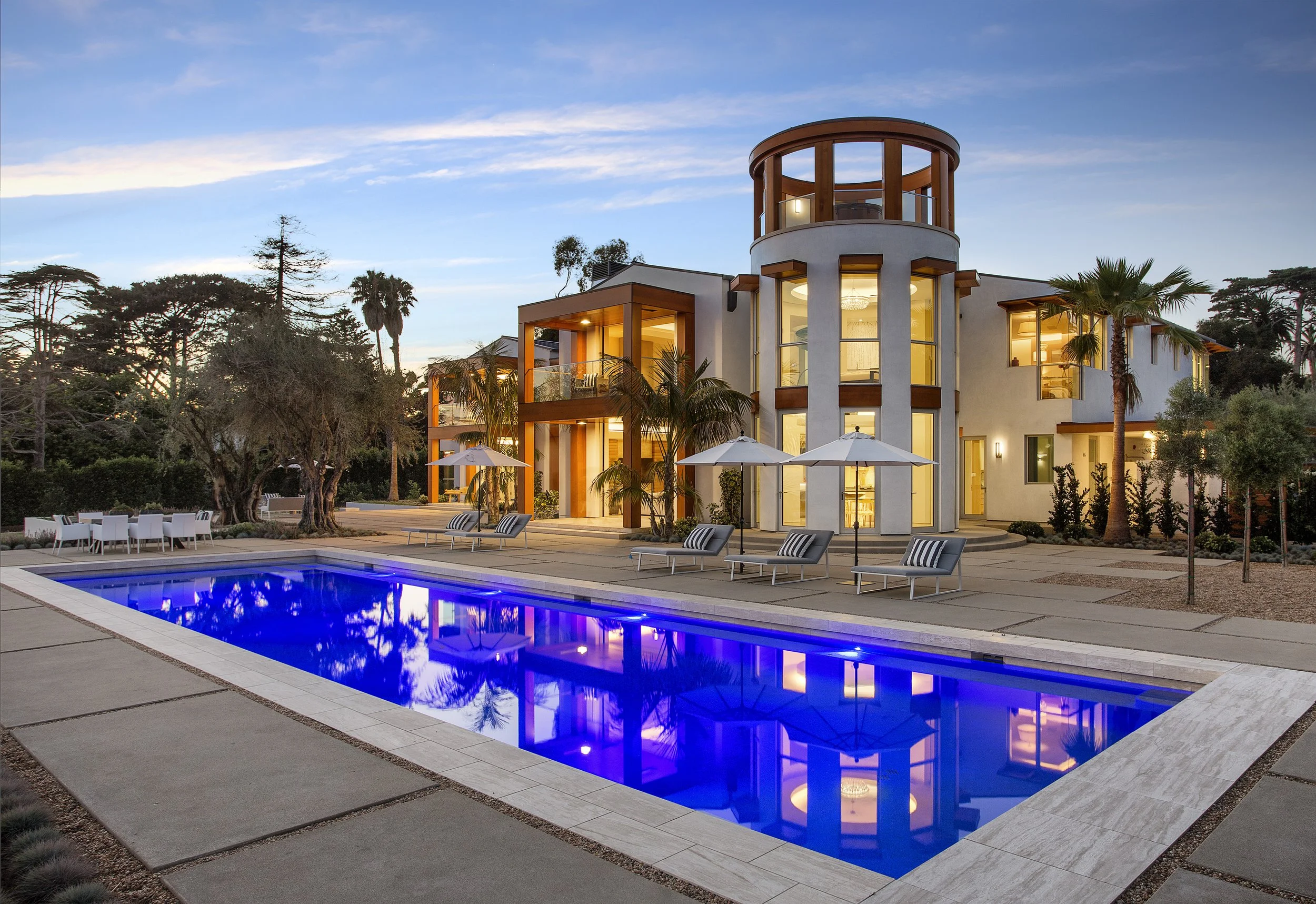 Modern luxury home with illuminated pool and large glass windows reflecting a contemporary architectural design.