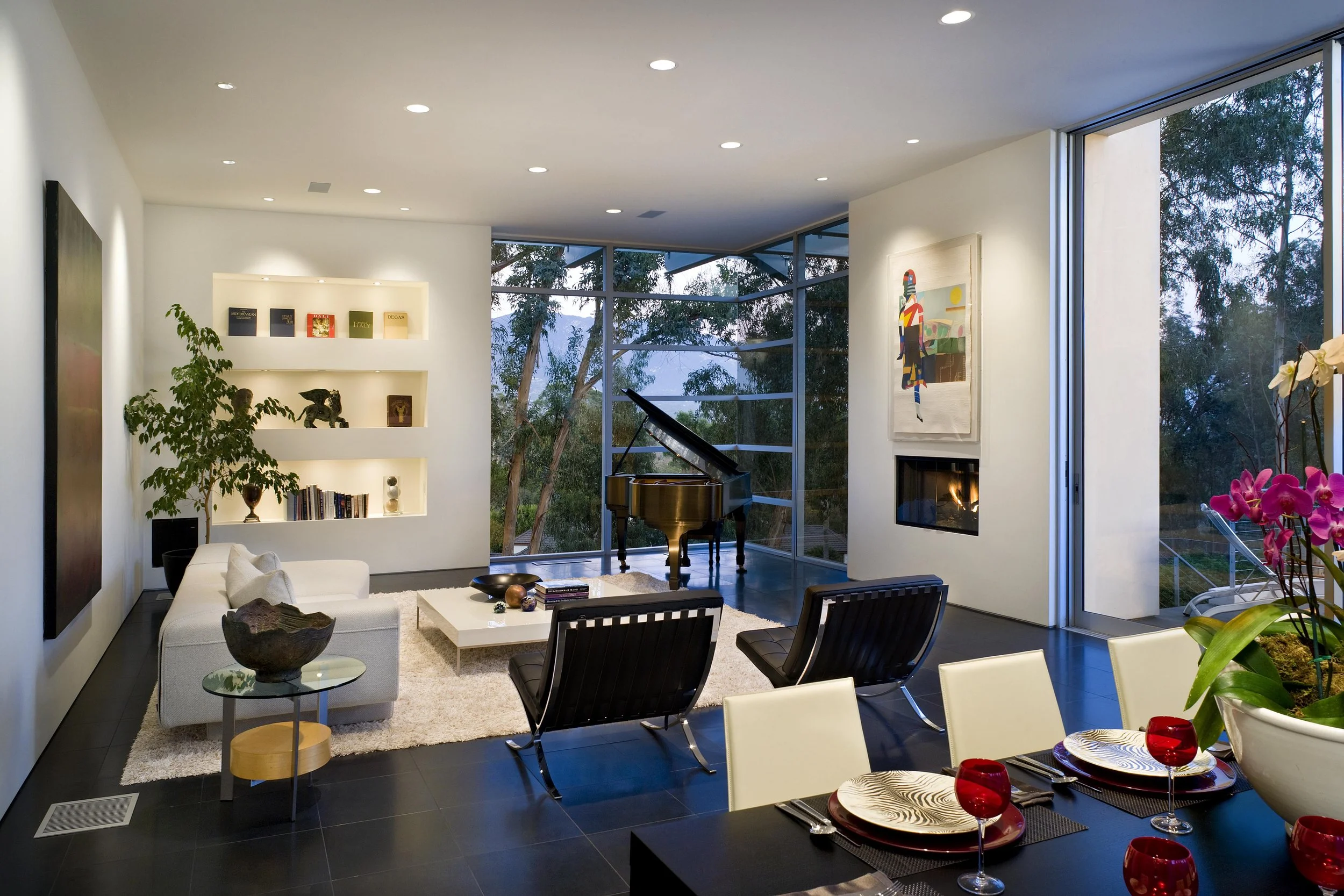 Modern living room with floor-to-ceiling glass windows at Woodly Road Residence, featuring a grand piano, minimalist décor, and forest views.