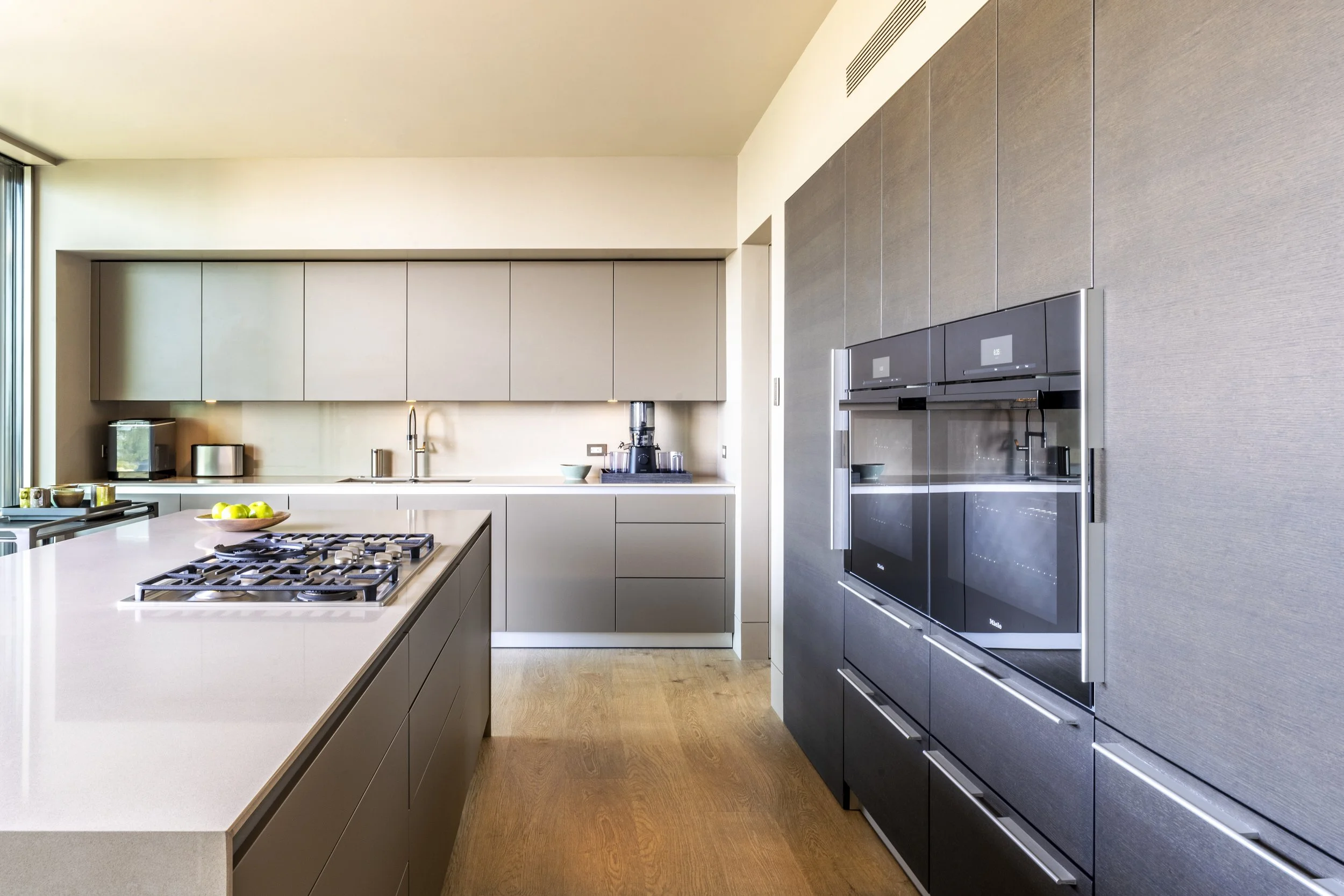Modern kitchen at Toro Canyon Residence by The Warner Group Architects, Inc., featuring sleek cabinetry, built-in appliances, and a large island with a gas cooktop, blending minimalist design with functionality.