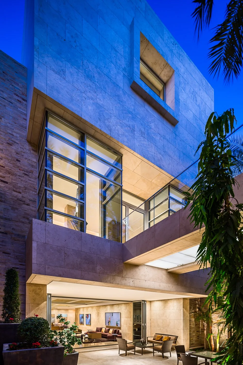 Modern luxury home exterior with large glass windows and stone facade, showcasing indoor-outdoor living space.