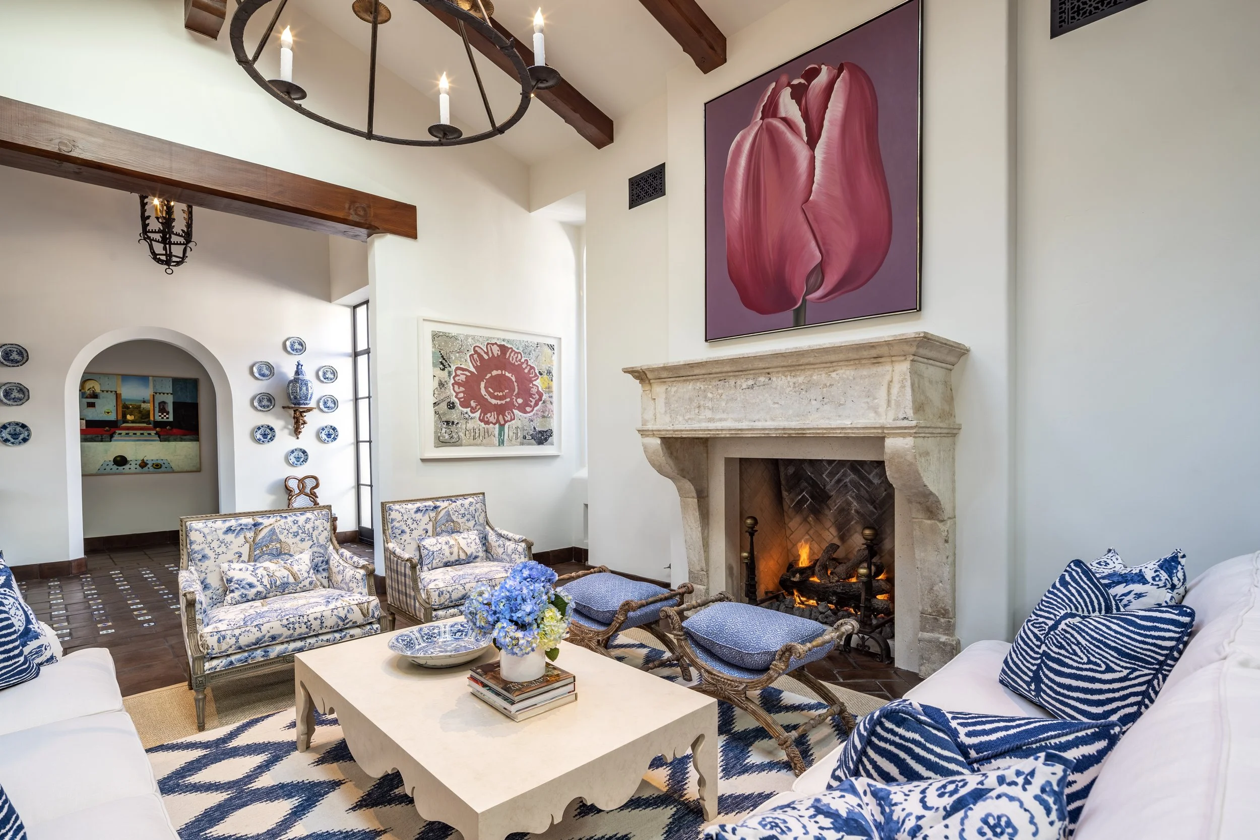 Elegant living room with wood-beamed ceiling and chandelier, featuring modern artwork in a Mediterranean-style home.