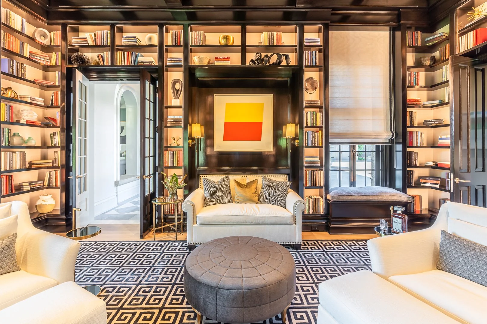 Luxurious living room with bookshelves, cozy seating, abstract art on wall, decorative rug, and French doors.