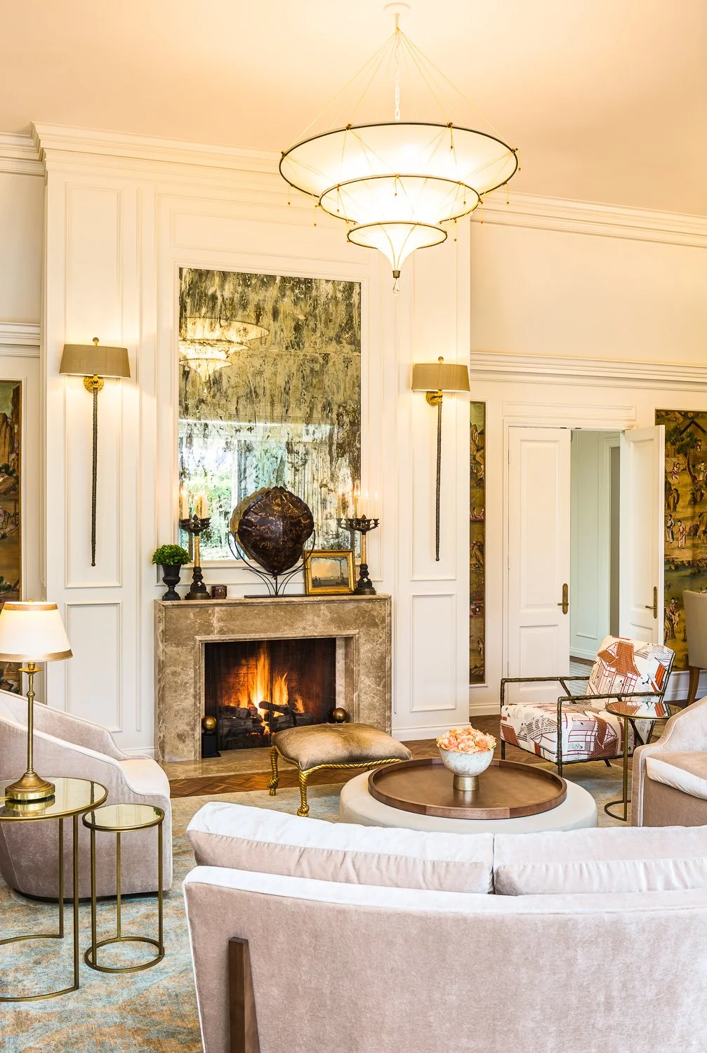 Elegant living room at Birnam Wood Residence, showcasing a luxurious fireplace with a grand mirror above, soft velvet chairs, and gold-accented décor.