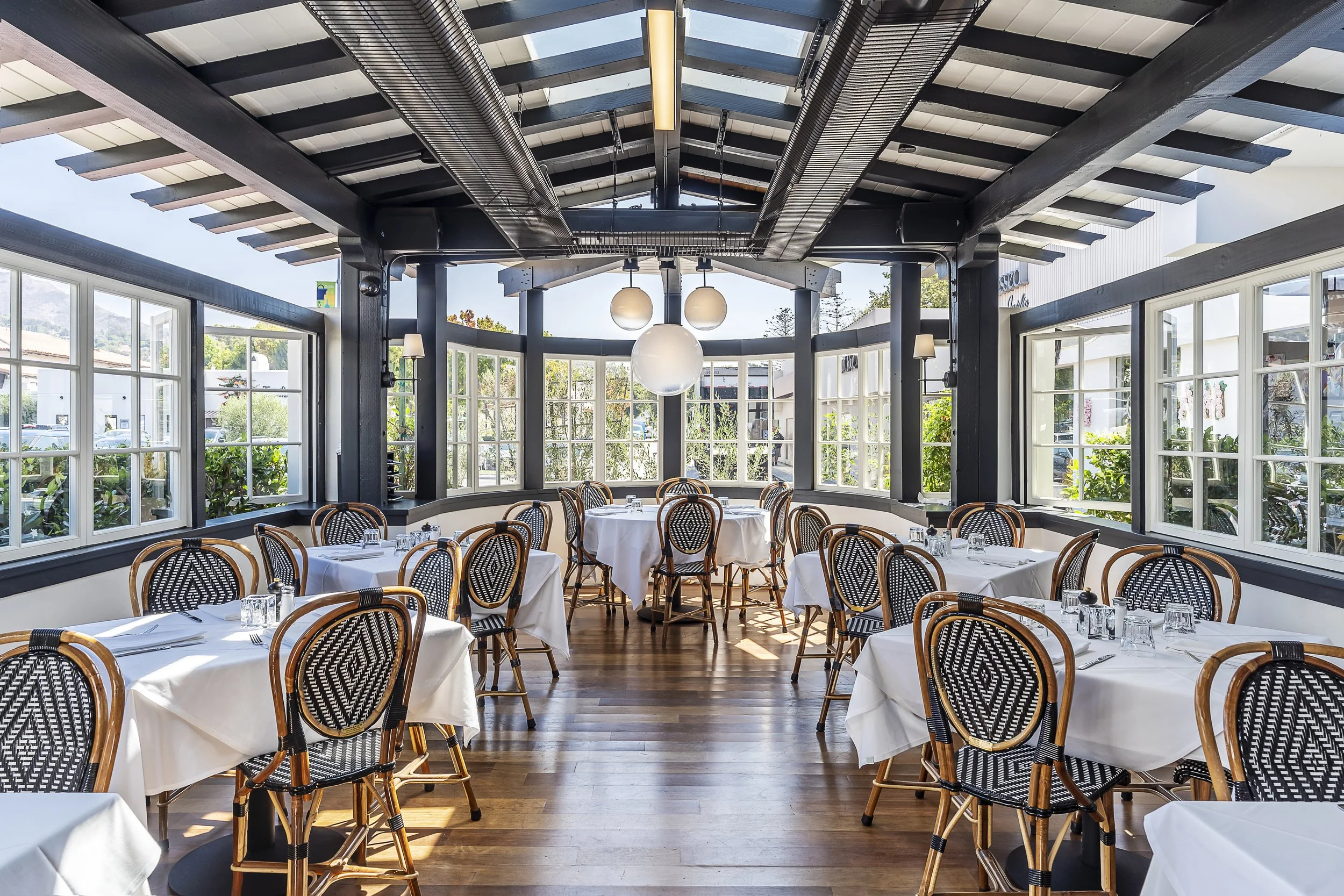 Bright dining area with woven chairs and large windows at Lucky’s Malibu, showcasing classic bistro-style decor with natural lighting.
