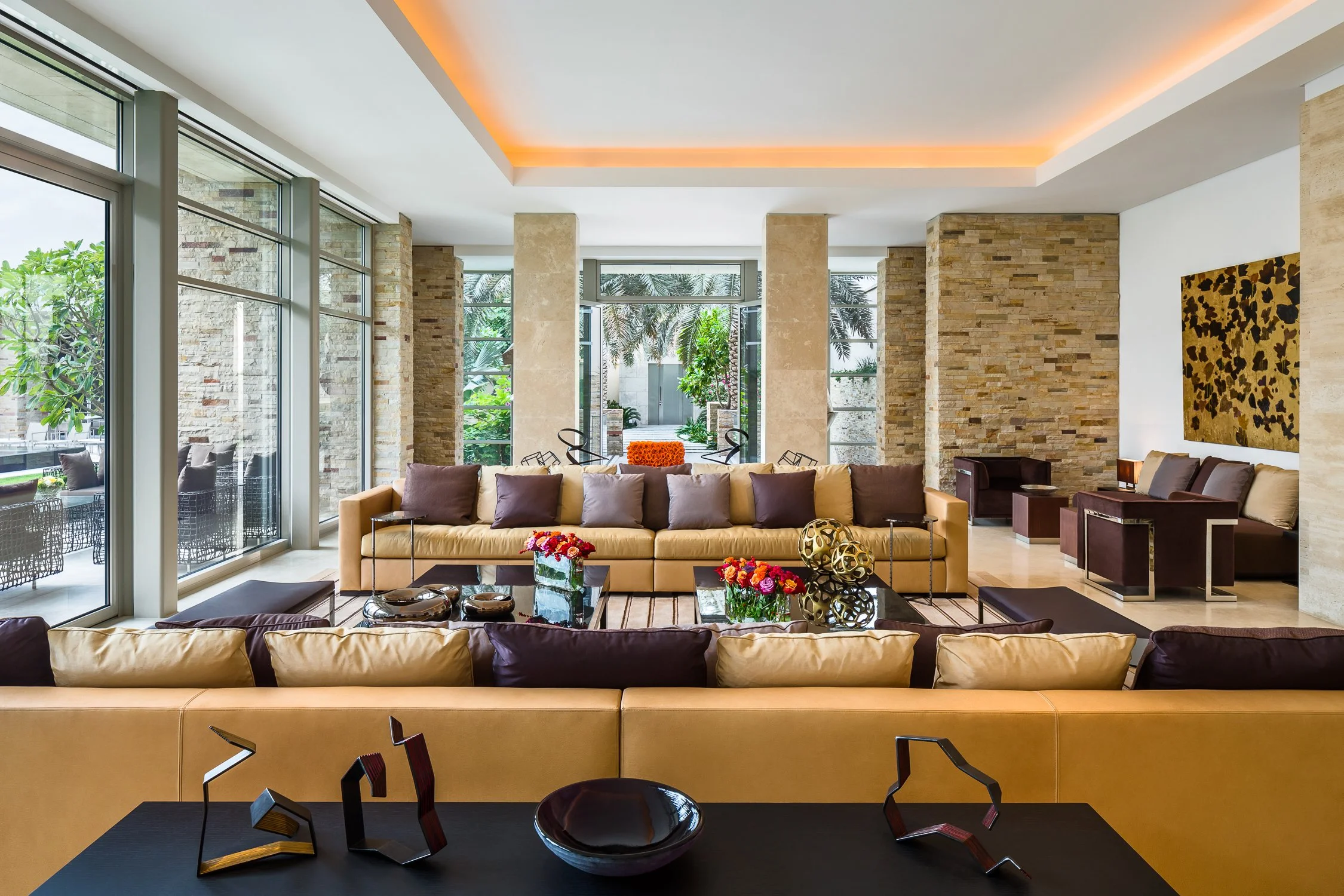 Modern living room with expansive glass walls, neutral-toned sofas, contemporary art, and accent lighting, creating an open, luxurious atmosphere at Kuwait Estate.