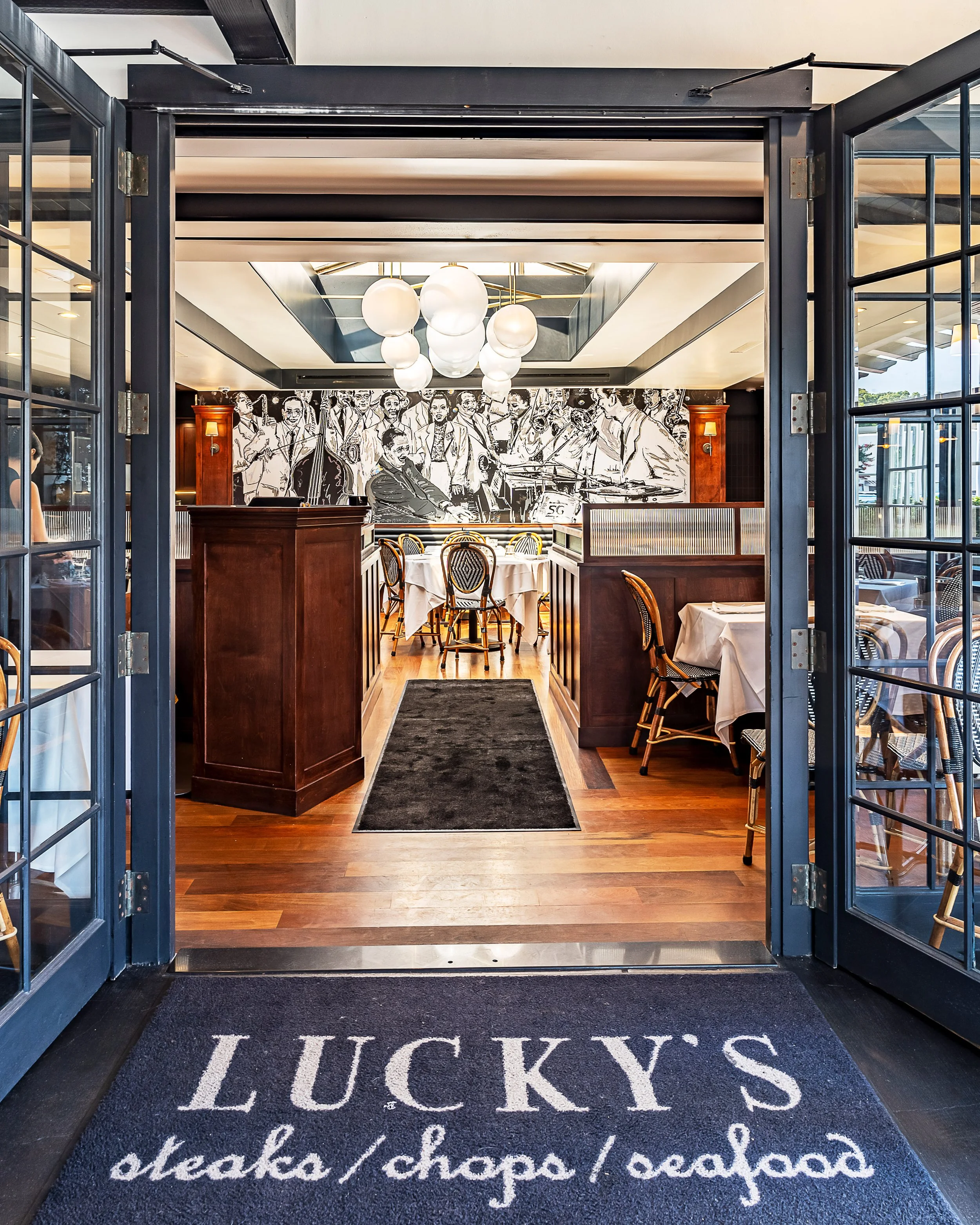 Entrance to Lucky's Malibu restaurant featuring elegant wood doors, jazz mural, and inviting dining atmosphere.