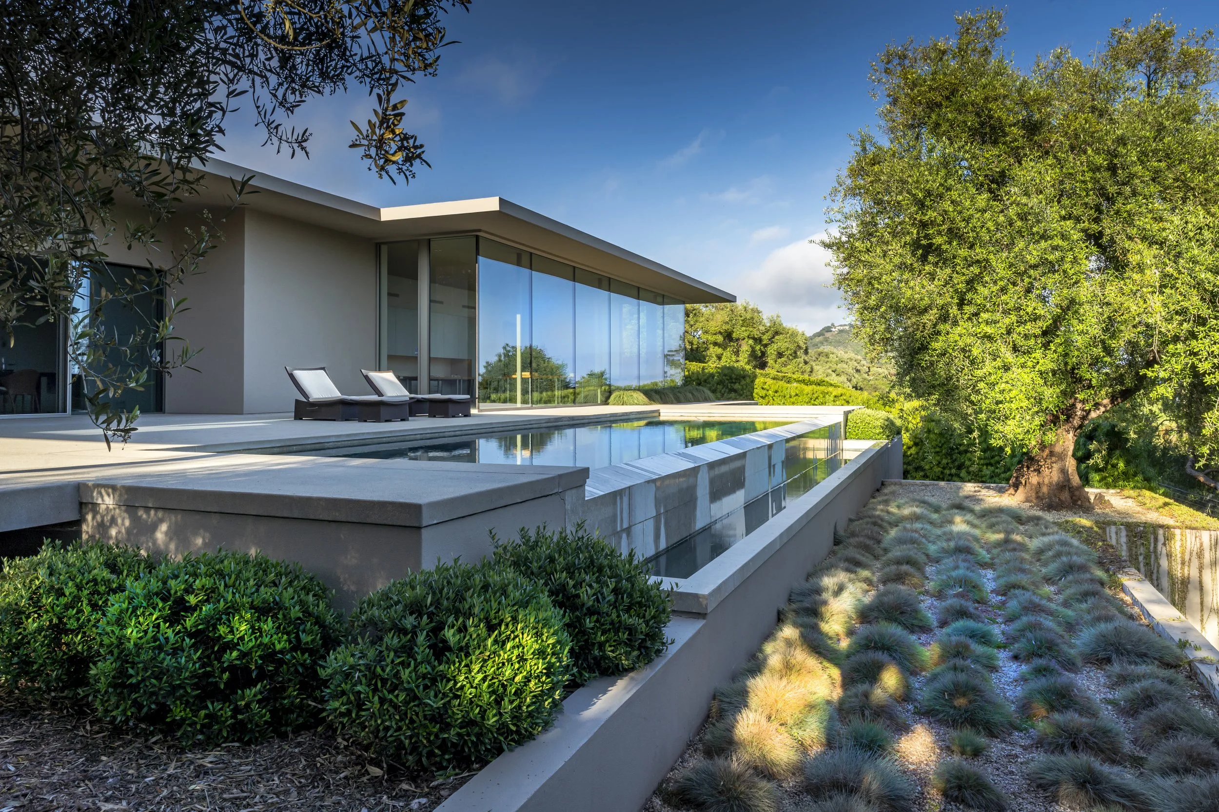 Modern outdoor living space at Toro Canyon Residence by The Warner Group Architects, Inc., featuring sleek architecture, a reflective infinity pool, and landscaped garden with lush greenery and mature trees.