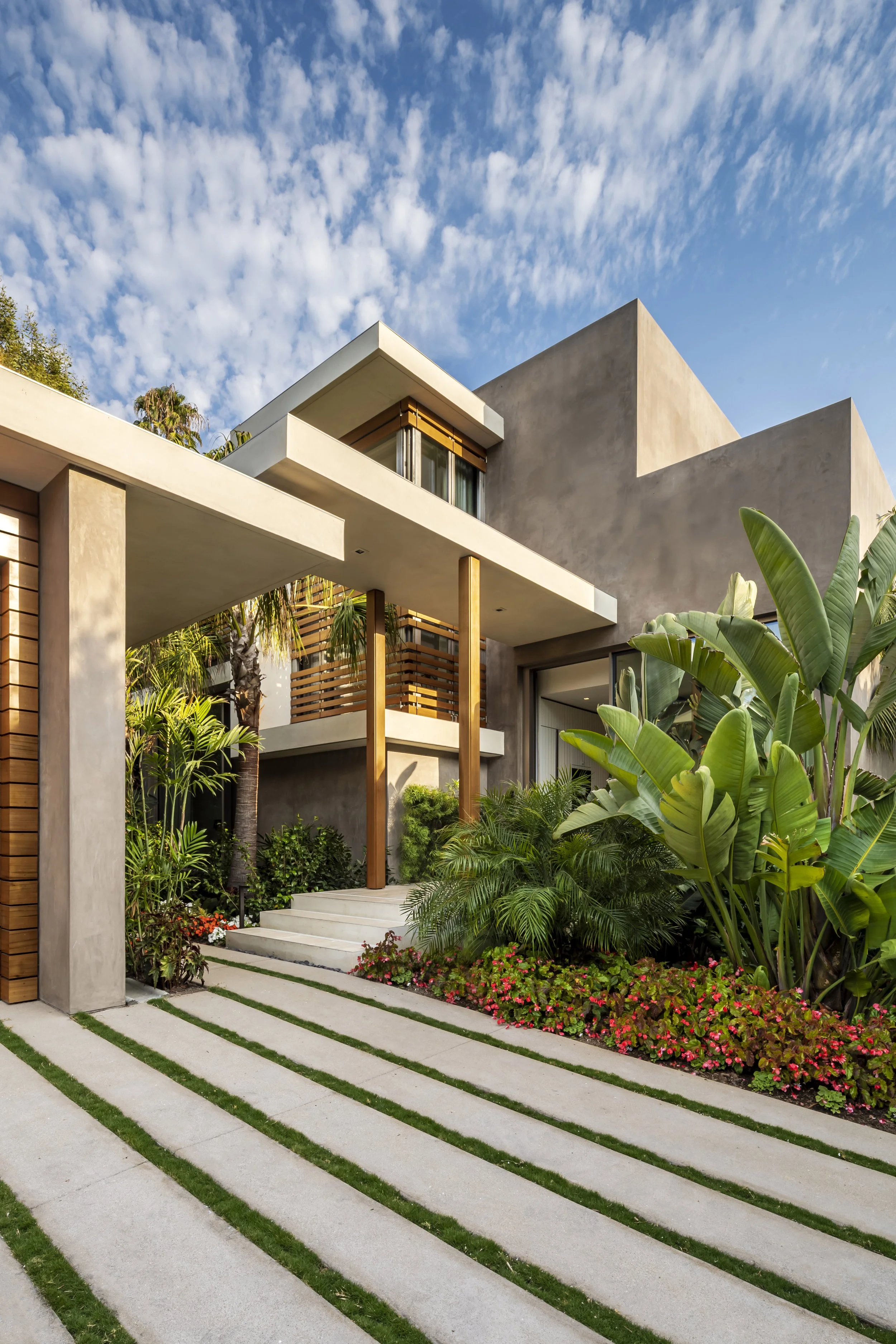 Modern house exterior with concrete pathway, tropical plants, and clear blue sky.