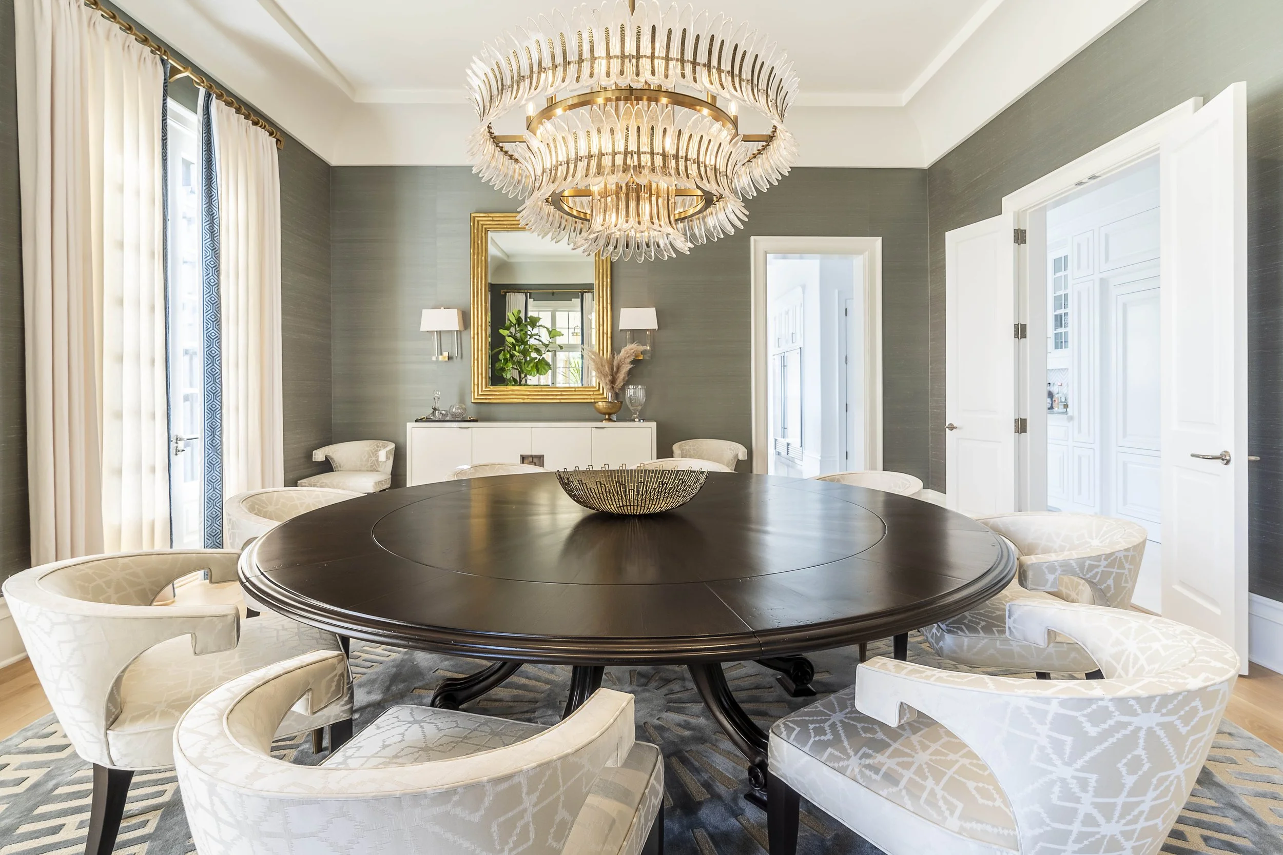 Elegant dining room with large round table, upholstered chairs, and a statement chandelier, designed by The Warner Group Architects, Inc.