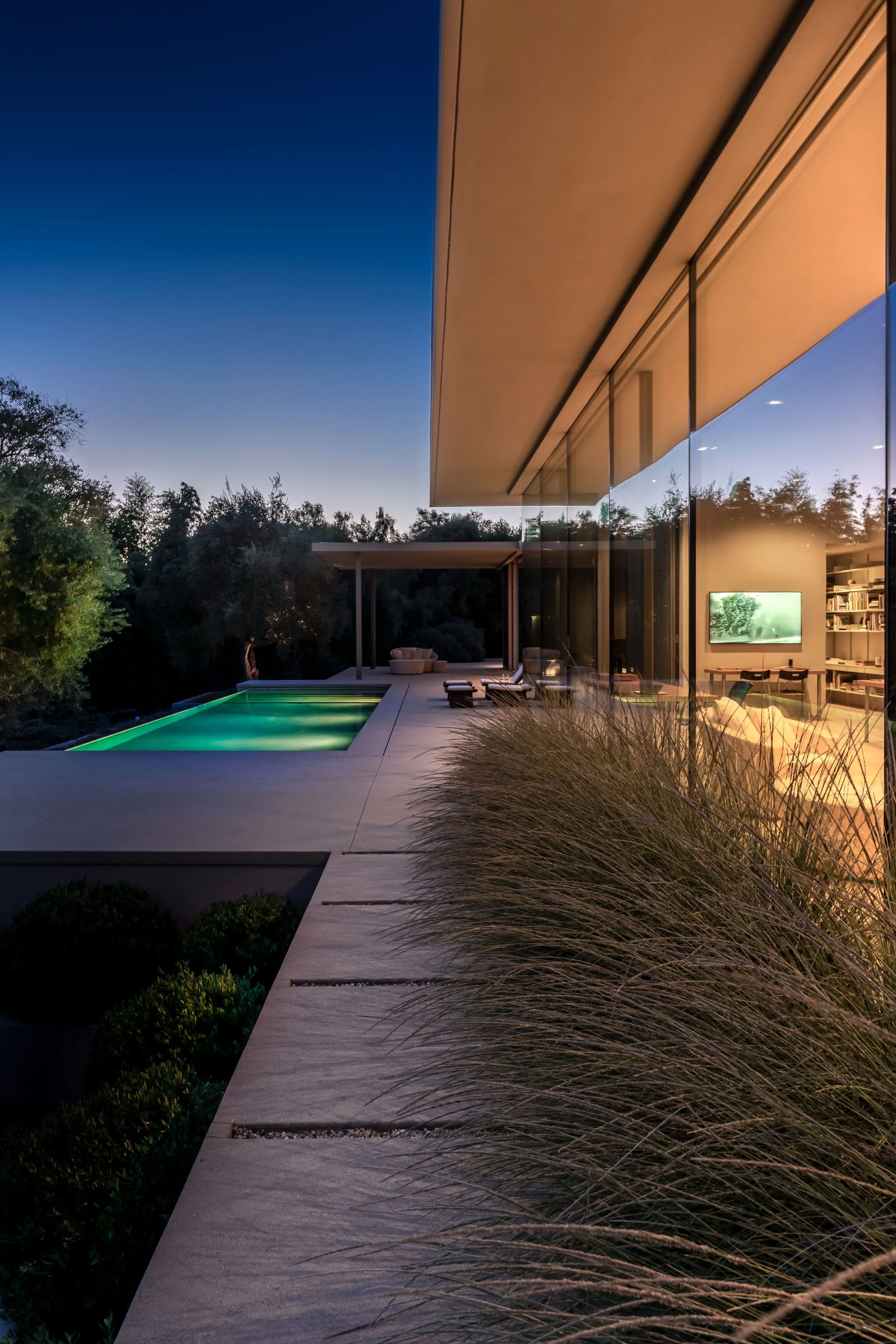 Modern luxury poolside at Toro Canyon Residence by The Warner Group Architects, Inc., featuring expansive glass walls, sleek architecture, and ambient evening lighting that seamlessly blends indoor and outdoor spaces.