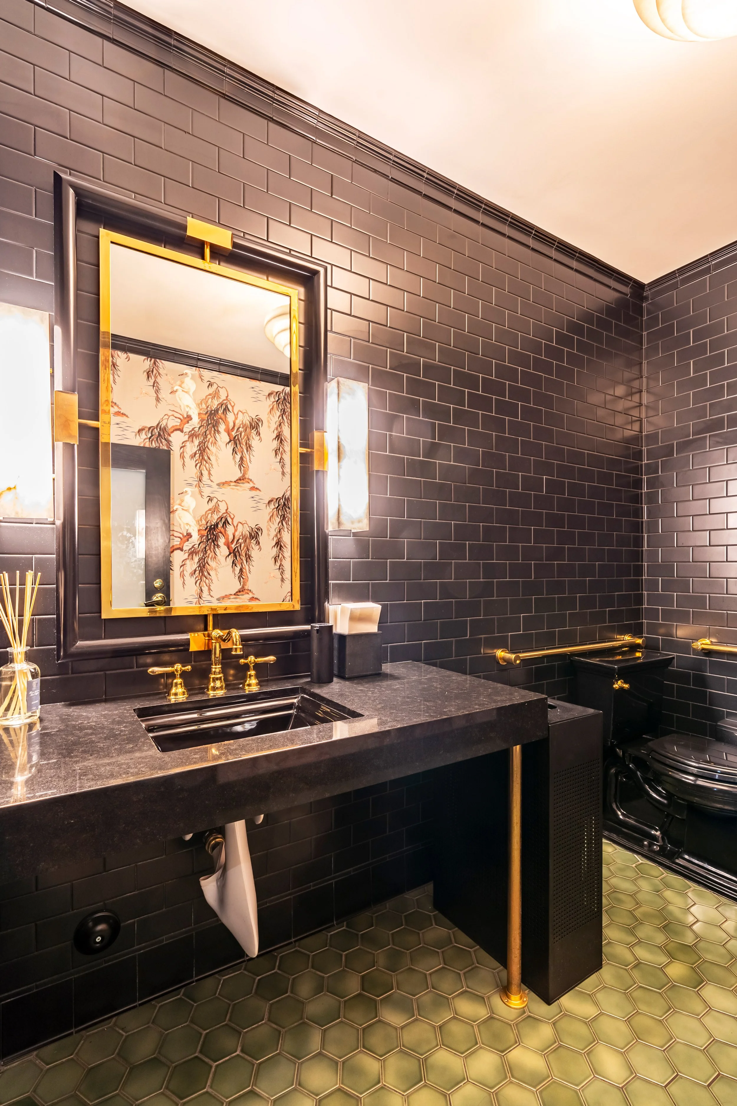 Elegant bathroom with black subway tiles, gold fixtures, hexagon floor tiles, and a decorative mirror at Lucky's Malibu.