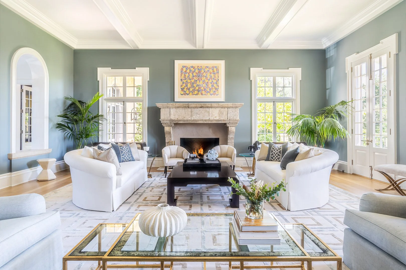 Spacious living room with stone fireplace, white sofas, and modern decor, featuring large windows and greenery, designed by The Warner Group Architects, Inc.